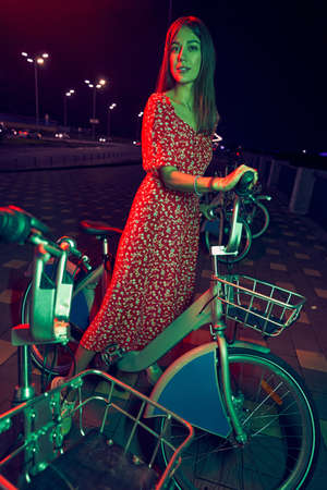 Woman with bike standing on the street at nightの写真素材