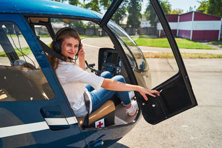 Pleased airwoman seated in chopper touching her noise-canceling headphonesの写真素材