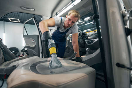 Worker dry cleans car seats from dirt using special equipmentの写真素材