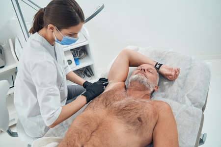 Male person receiving underarm injection in cosmetology clinicの写真素材