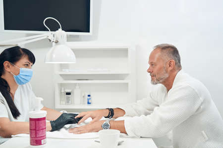 Manicurist in medical mask doing manicure for man in salonの写真素材