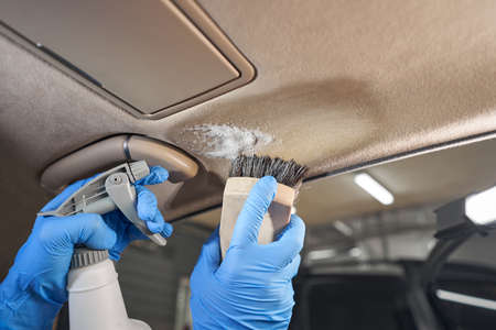Car wash worker cleaning car interior with brushの写真素材