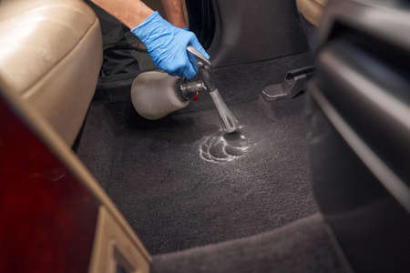 Service worker cleaning automobile with washing foam
