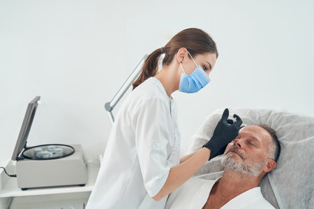 Doctor in medical mask making injection in man forehead