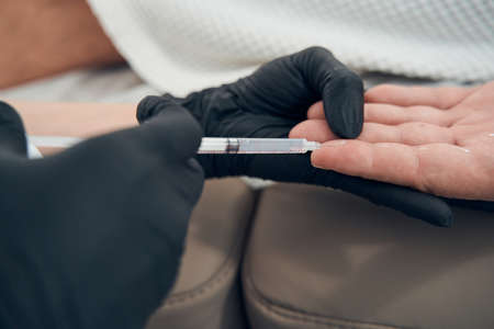 Doctor cosmetologist making injection into male fingerの写真素材