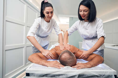 Smiling masseuses massaging man back in spa salonの写真素材