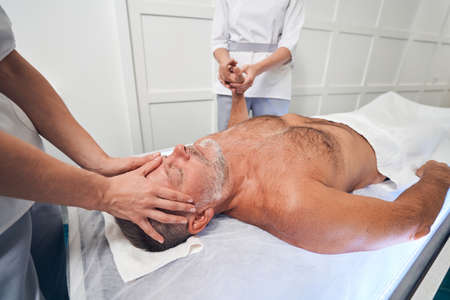 Man receiving scalp and hand massage in spa salonの写真素材