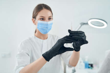 Beautician in medical mask preparing syringe for procedureの写真素材