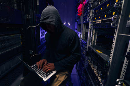 Focused hacker typing on laptop in server roomの写真素材