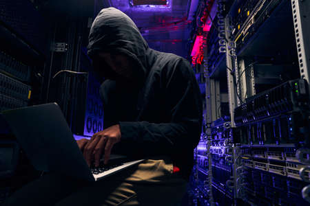 Hacker seated in server room launching cyberattack on laptopの写真素材
