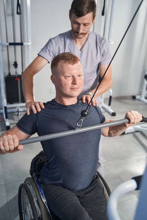 Physiotherapist help wheelchair man at recreation center. Back rehab
