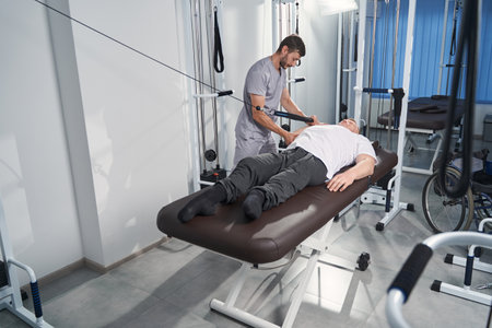 Man pulls resistance band on massage table with physiotherapistの写真素材