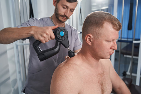 Specialist massages back with percussion tool of man with disability