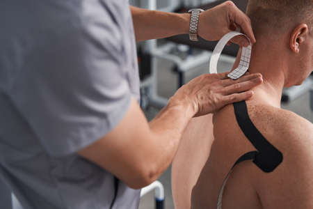 Physiotherapist applying black kinesio tape to man back, neck close upの写真素材