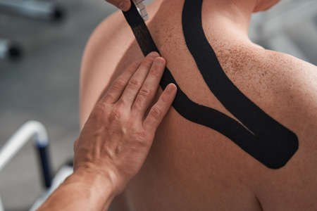 Physiotherapist treats patient shoulder pain with medical tape close up