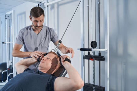 Handicapped man stretches strap on strength-training machine