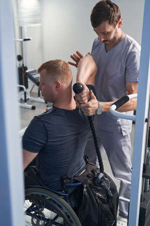 Doctor helps wheelchair man pull strength tether with hand back view
