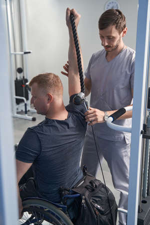 Young man exercises physio therapy. Doctor helps patient in wheelchairの写真素材