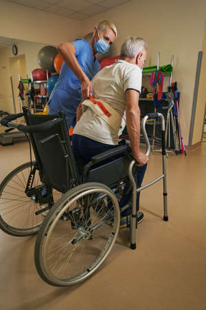 Therapist assisting mature patient in using walker in rehab center