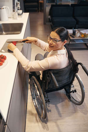 Smiling female with disability cooking meals at homeの写真素材
