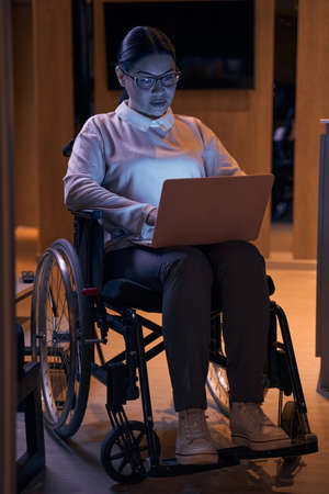 Asian businesswoman on wheelchair using laptop indoorsの写真素材