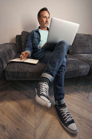 Mature man on sofa with laptop and sketchbookの写真素材
