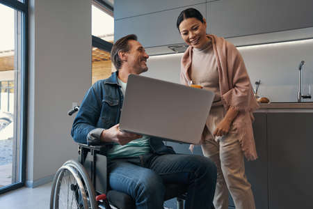 Jolly man with paraplegia and his wife watching laptop