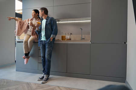 Happy couple with drinks communicating in kitchen