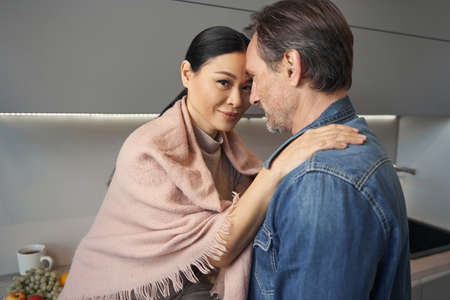 Happy Asian woman embracing husband in kitchen
