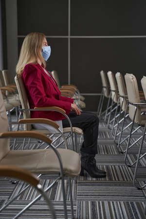 Woman in mask sitting on chair inside airport terminal