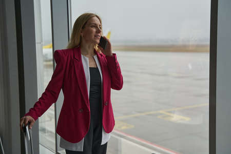 Female having a chat on smartphone near airport terminal windowの写真素材