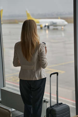 Adult standing before window with coffee and baggageの写真素材