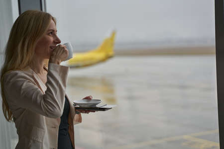 Traveler drinking coffee from cup near business terminal windowの写真素材
