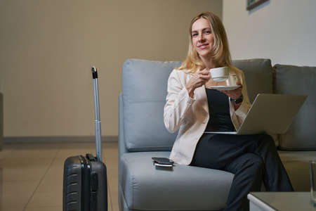 Woman with coffee smiling to camera from sofa in hotelの写真素材