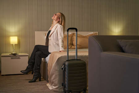 Happy woman sitting on bed in hotel and looking upの写真素材