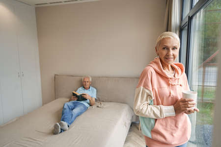 Positive delighted blonde woman standing near windowの写真素材
