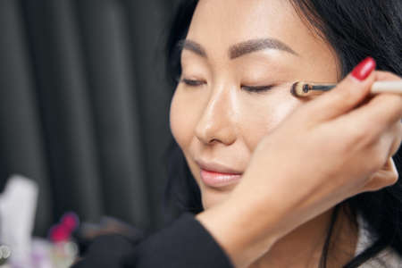 Happy Asian female receiving professional visage with luxury cosmetics in salonの写真素材