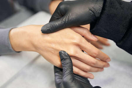 Detail photo of arms in black gloves making nail treatment in nail salonの写真素材
