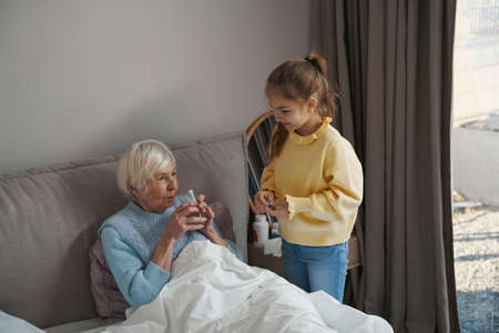 Attentive granddaughter helping nurse grandma back to healthの写真素材