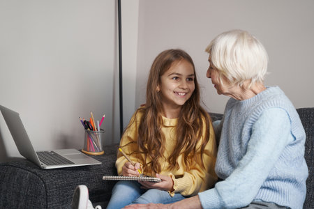 Adorable granddaughter and grandma doing homework together at homeの写真素材