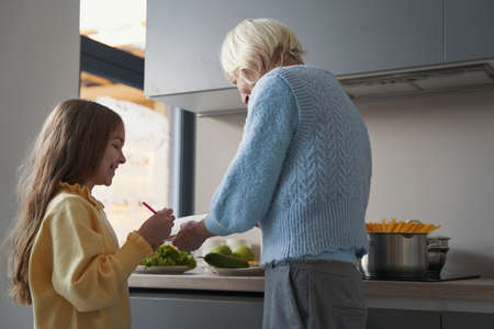 Joyous child cooking together with her grandma in the kitchen