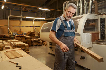 Competent craftsman measuring width of wooden bar