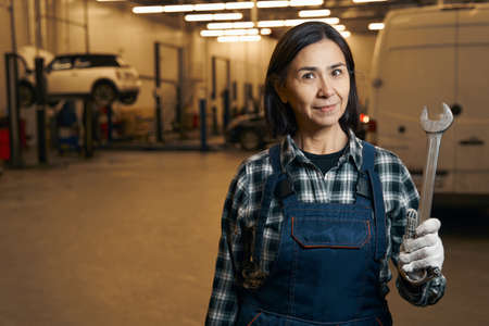 Attractive repairwoman holding a mechanic wrench at car service shopの写真素材