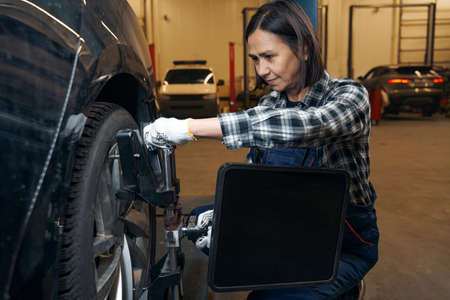 Friendly brunette woman replacing a tyre on a car at service stationの写真素材