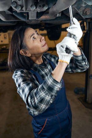 Focused female car technician working hard at fixing a vehicleの写真素材