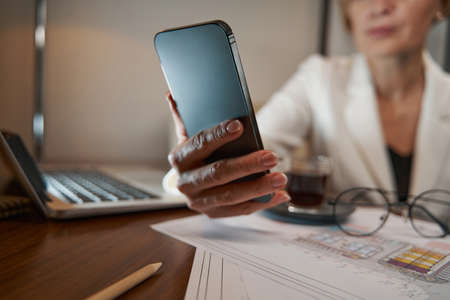 Businesswoman holding smartphone while sitting at table in hotelの写真素材
