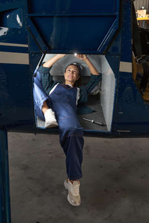 Charming woman in overall using flashlight while modernization parts of airplaneの写真素材