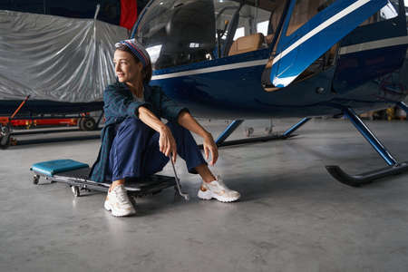 Tired elegant female engineer is resting after the work with aircraft in hangarの写真素材
