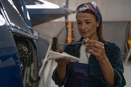 Attractive female engineer analyzing airplane parts in hangarの写真素材