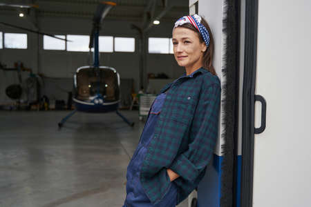Brunette female in overall posing at the photo camera in aviation garageの写真素材